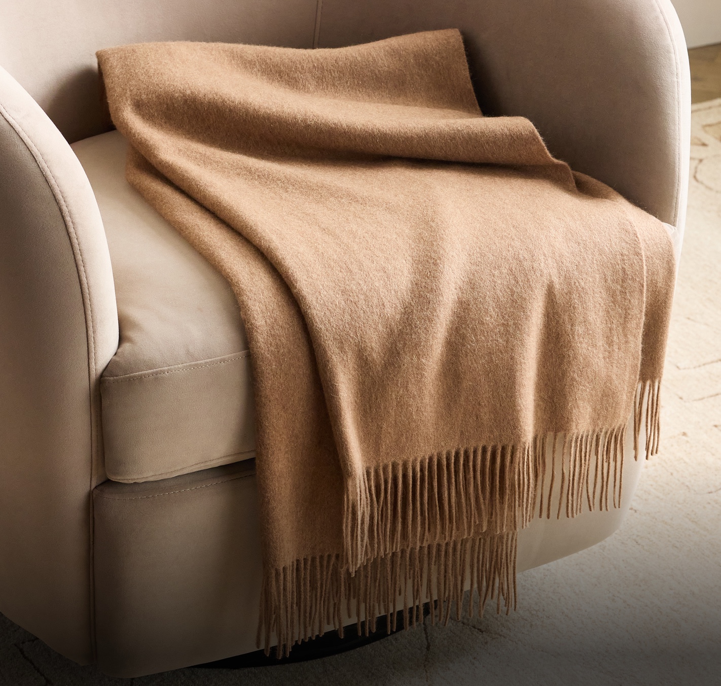 A camel cashmere throw with a long fringe draped over a cream swivel armchair — Container 2 banner, UK homepage, 22 Oct 2026