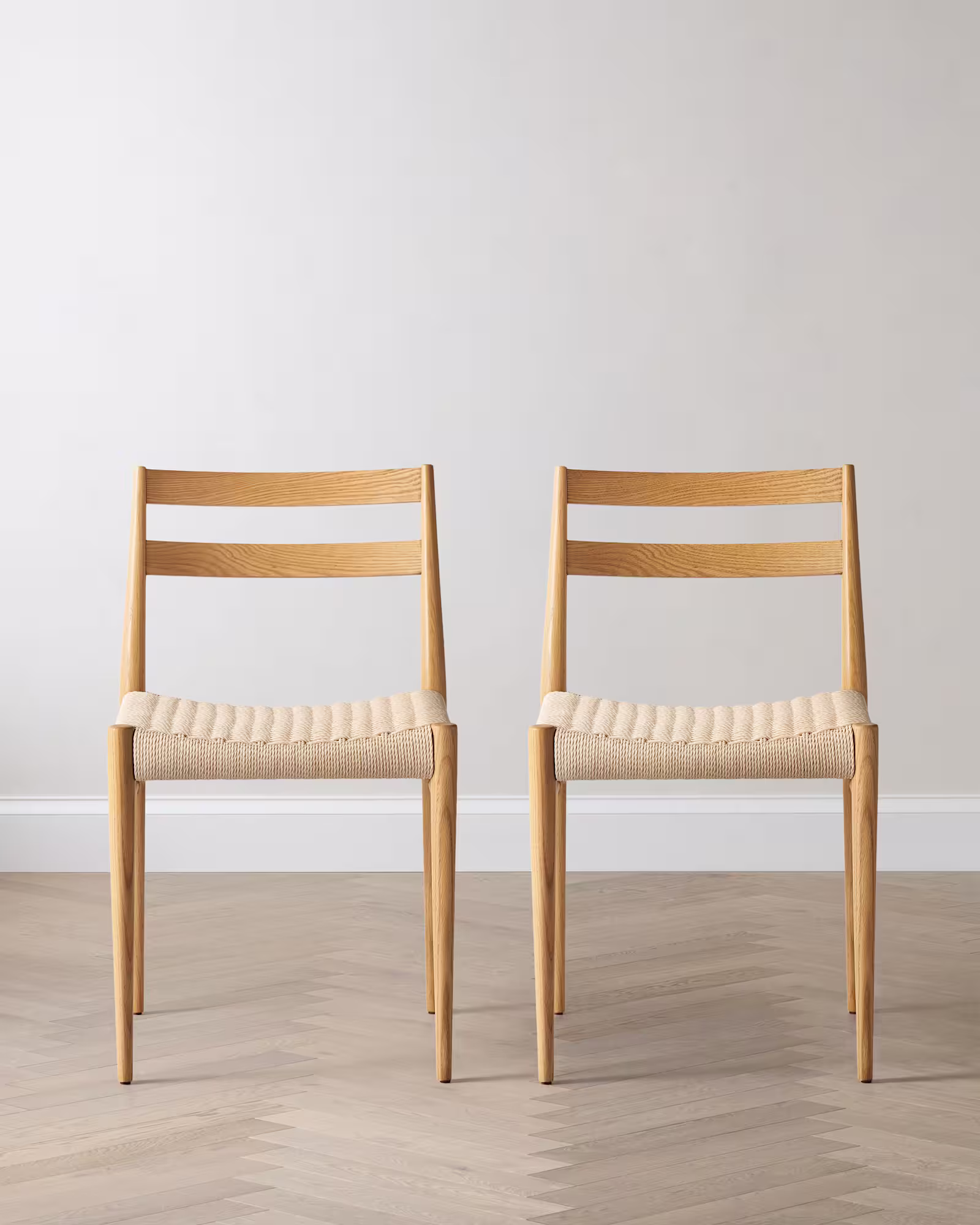 Two solid oak dining chairs with paper cord seats on a light floor.
