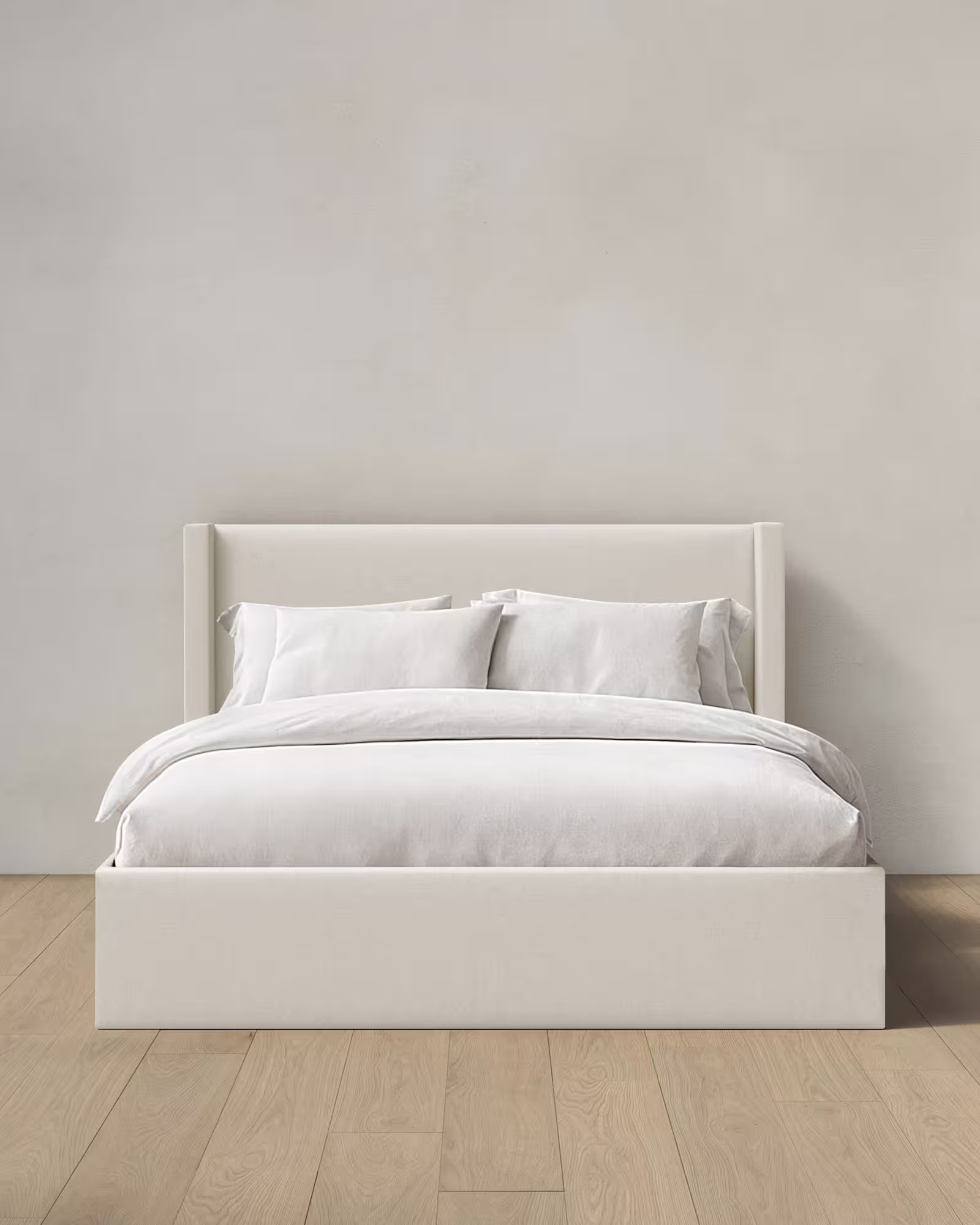 White wingback bed with white linens on a bedroom floor.